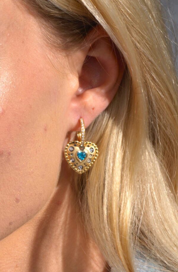 A woman wearing gold earrings with blue stones.
