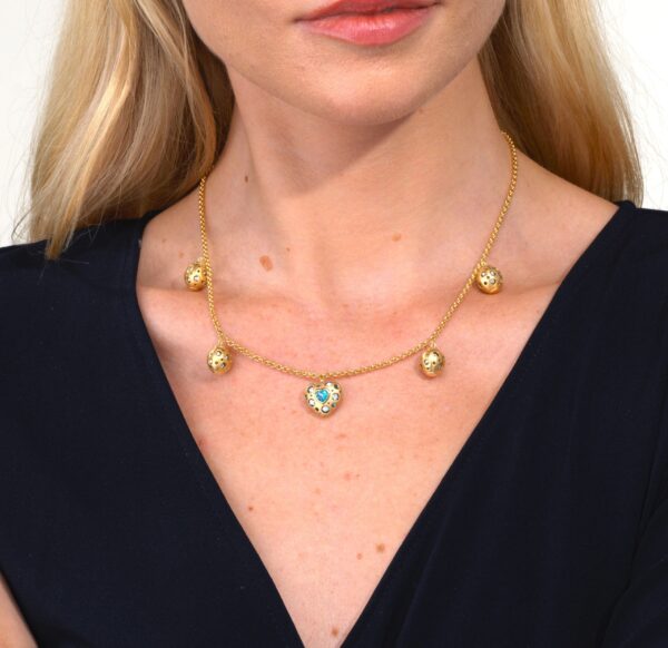 A woman wearing a necklace with gold balls and a blue stone.