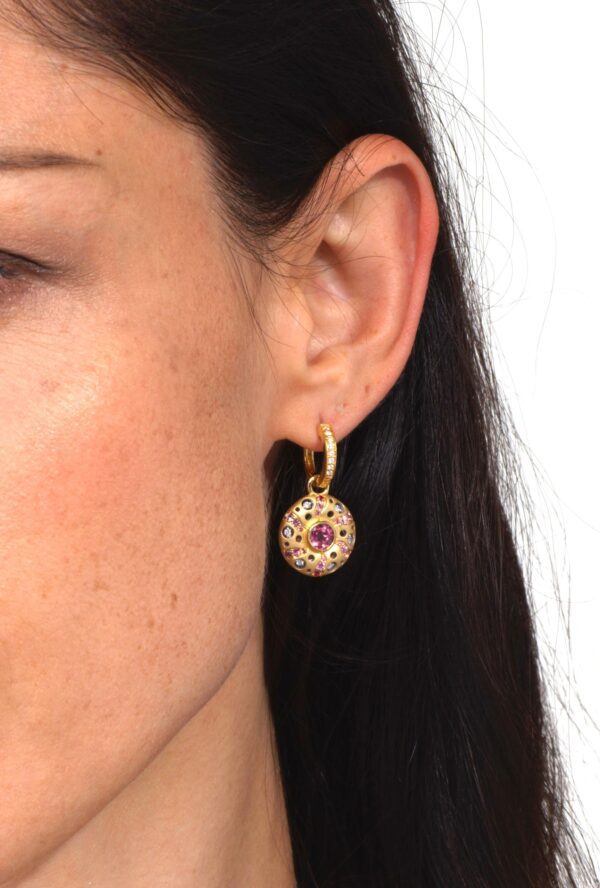 A woman wearing gold earrings with pink stones.